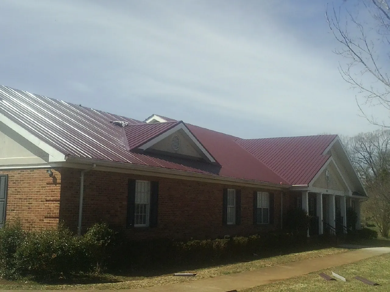 Red metal roof with gabled entries on a long brick building, from a Hail Damage Roof Repair job in Gordon