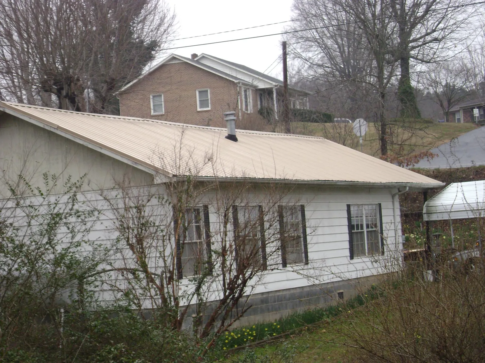 Tan metal roof on a white sided house set into a hillside — Commercial Roofing by Roofing Brothers in Gordon